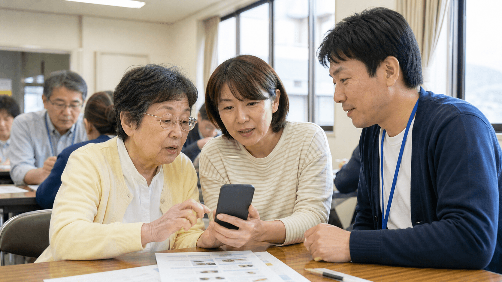 地域のスマホ教室で、高齢の参加者が家族と一緒に無地のスマートフォンを見ながら、講師の説明を受けている様子