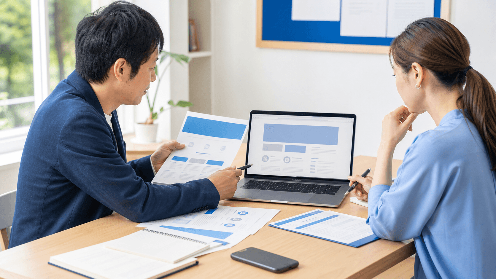 地域企業の担当者2人が、印刷したサービス資料とノートPC上のホームページ下書きを見比べながら、Web本文に載せる要点を相談している様子