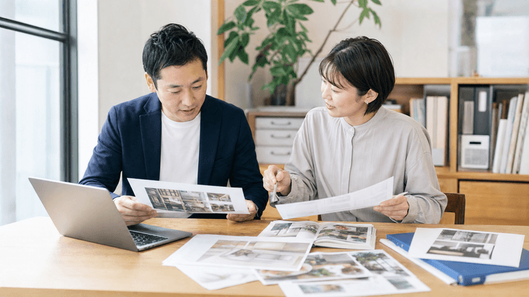 徳島の中小企業の担当者が、ノートPCの横に商品写真や印刷資料を広げ、ホームページ公開前の更新準備を打ち合わせている様子